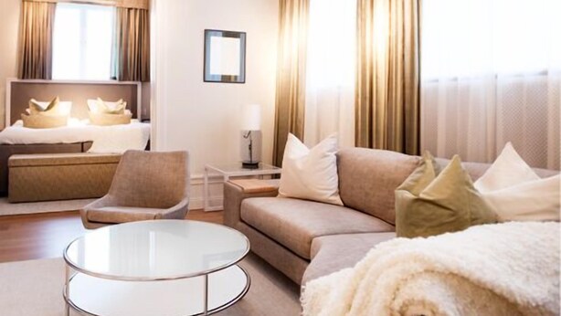 A hotel room with a bed, a sofa, a chair, a small table, and a large window with curtains. - Hotel Villa Anna (Uppsala)