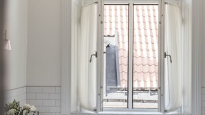 A modern bathroom with a large window, a wooden bench, and a sink with a vase of flowers. - Hotel Villa Anna (Uppsala)