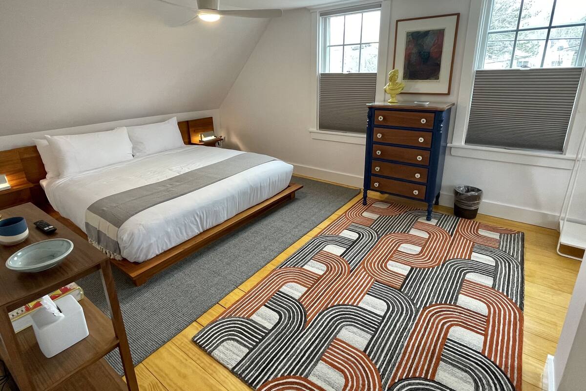 A bedroom with a bed, bedside table, dresser, windows, and a ceiling fan.