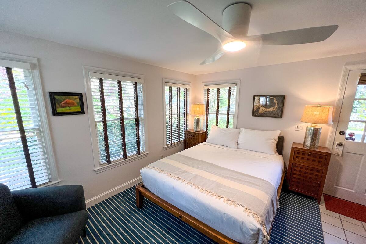 A bedroom with a bed, a chair, a nightstand, and a ceiling fan.