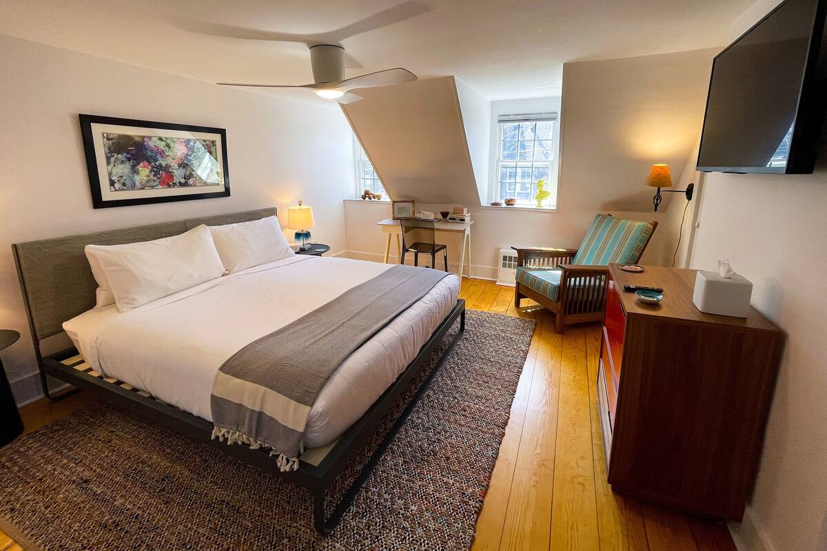A modern hotel room with a large bed, a desk, a chair, and a TV.