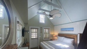 Une chambre à coucher avec un lit, un ventilateur de plafond, un grand miroir et une fenêtre avec des stores.