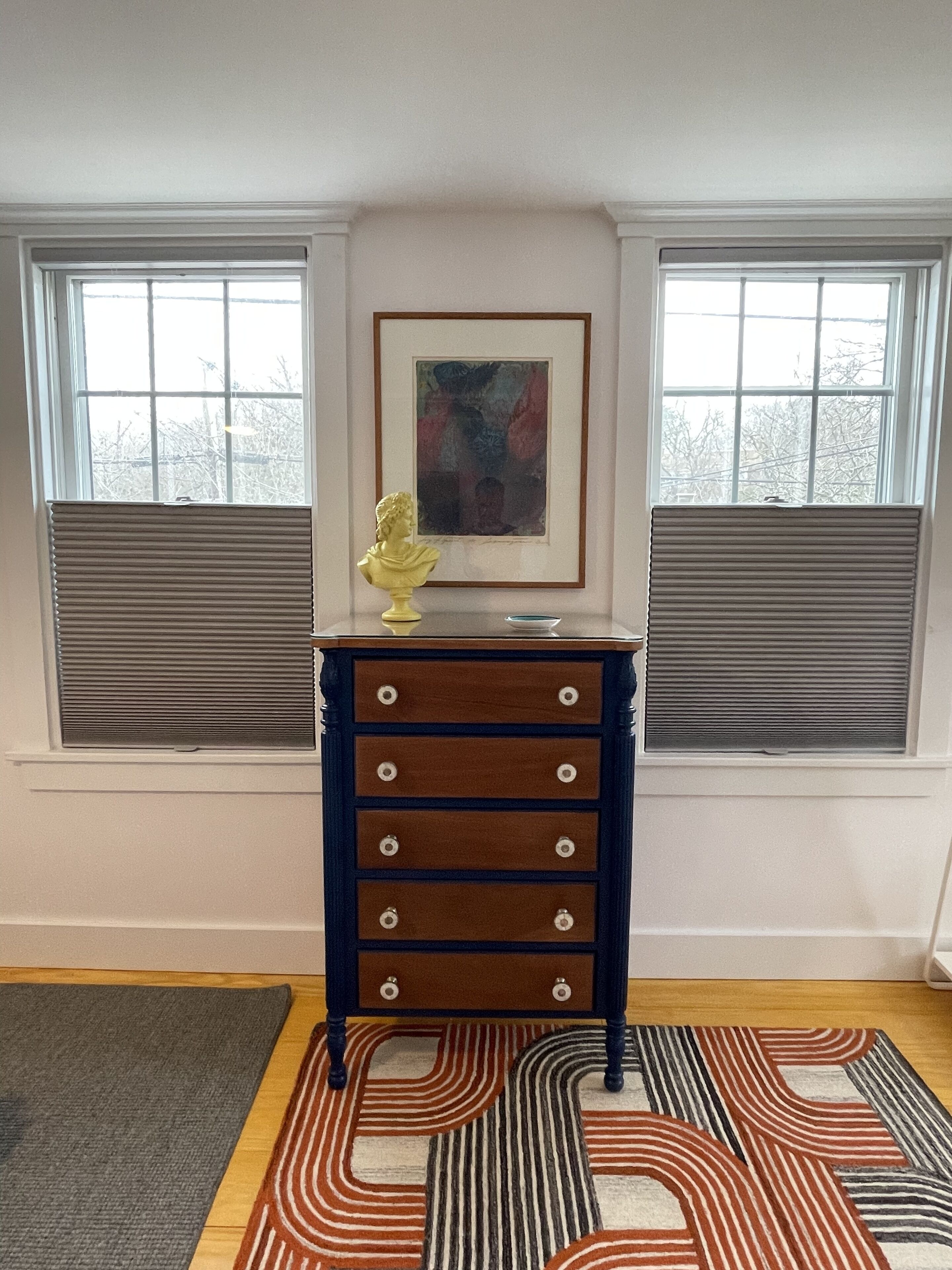 A room with a wooden dresser, a framed abstract painting, and a sculpture on top.