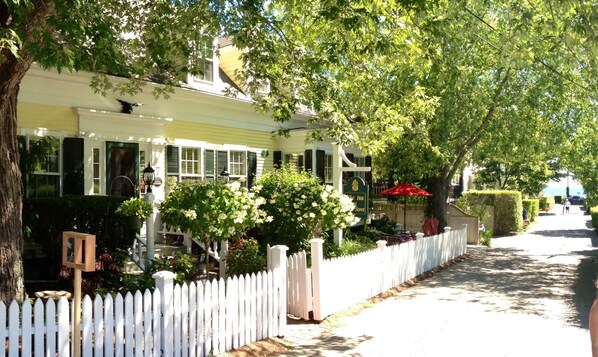 A row of yellow houses with green shutters, white picket fences, and lush greenery.