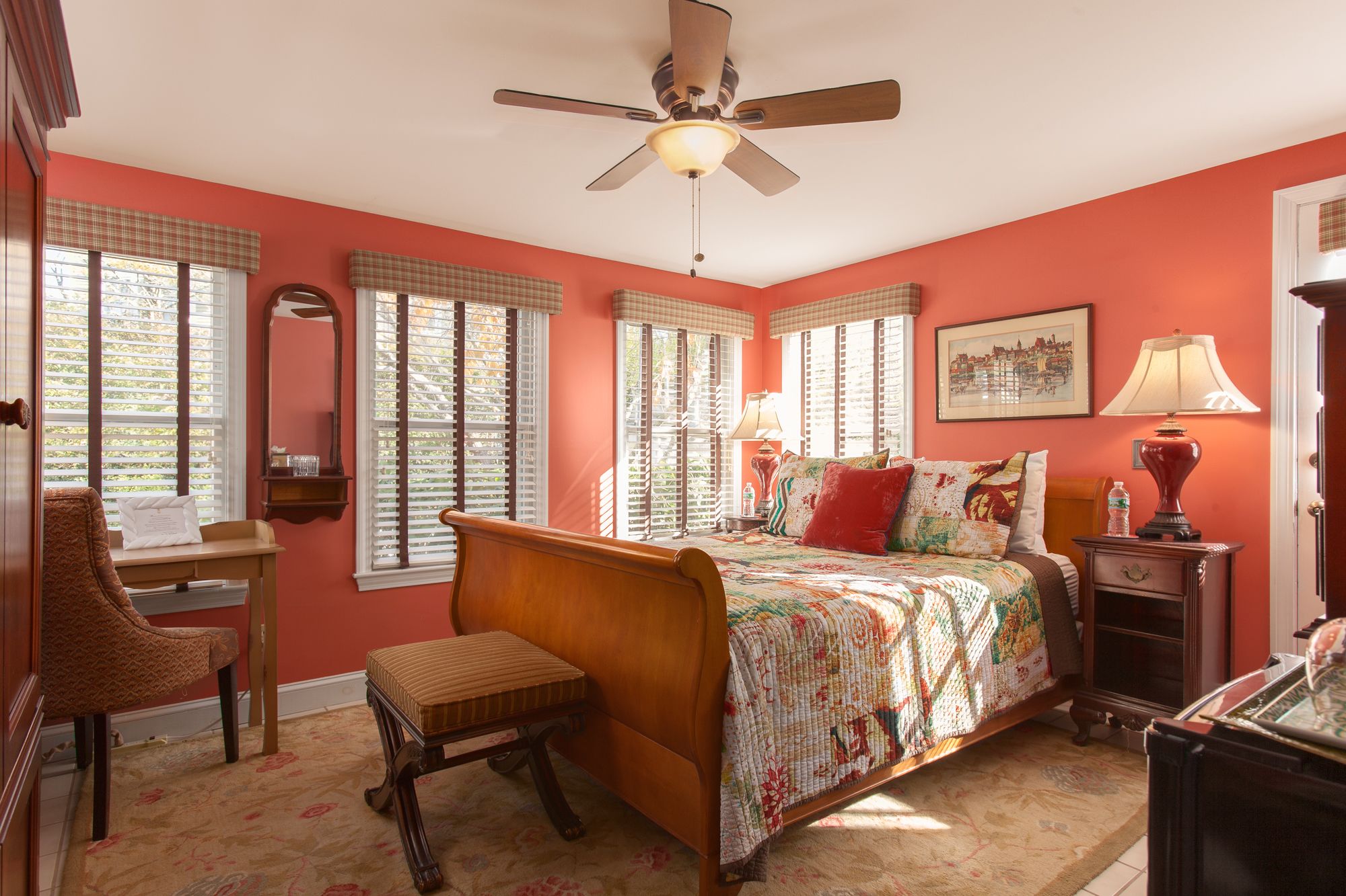 A bedroom with a bed, a chair, a desk, a lamp, and a ceiling fan.