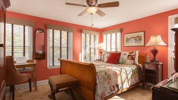 A bedroom with a bed, a chair, a desk, a lamp, and a ceiling fan.