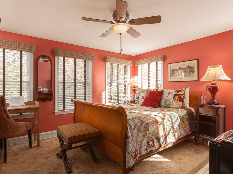 A bedroom with a bed, a chair, a desk, a lamp, and a ceiling fan.