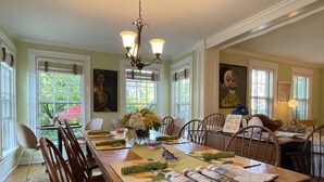 Une salle à manger avec une longue table en bois, des chaises, un lustre et des œuvres d’art accrochées aux murs.