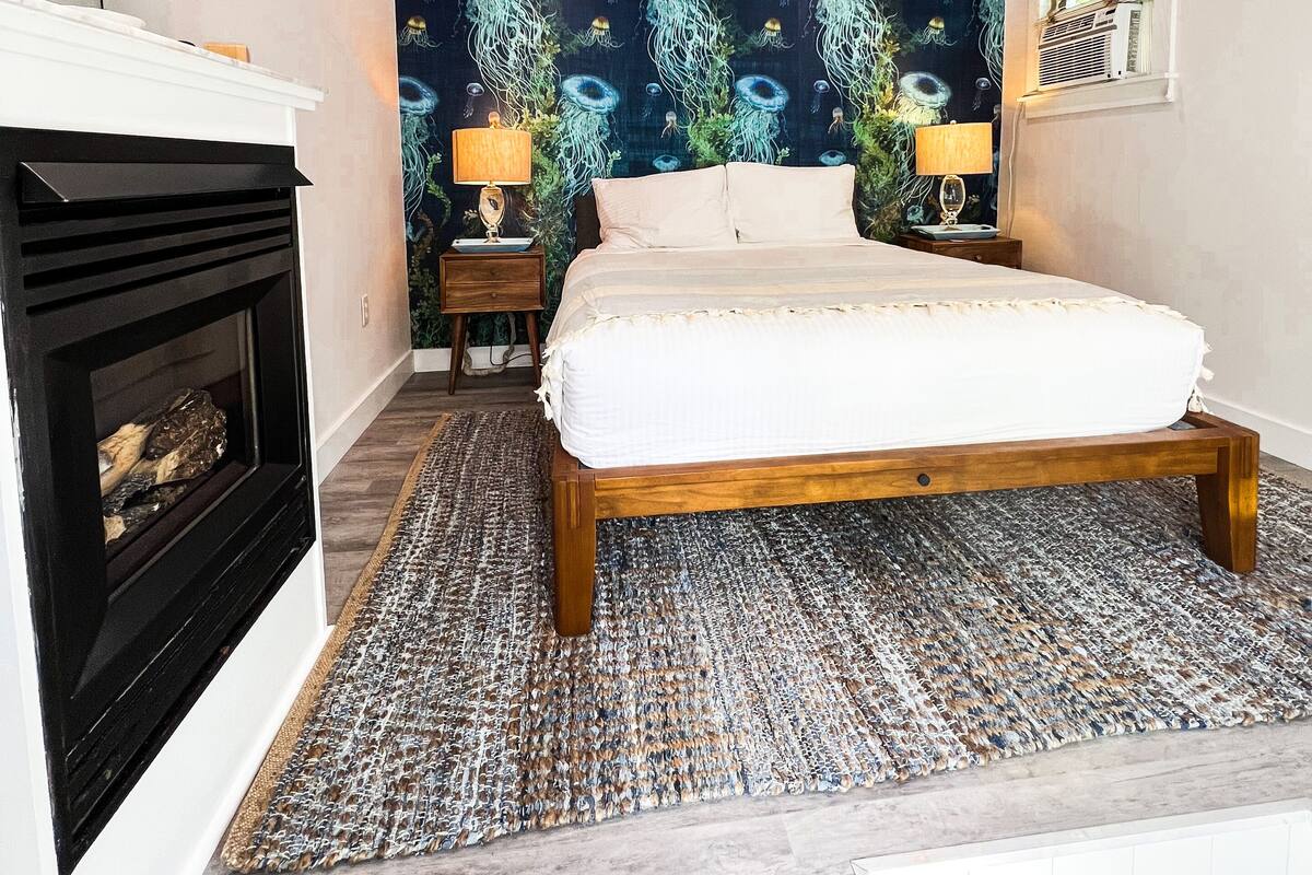 A bedroom with a bed, a fireplace, a ceiling fan, and a wall with a marine life wallpaper.