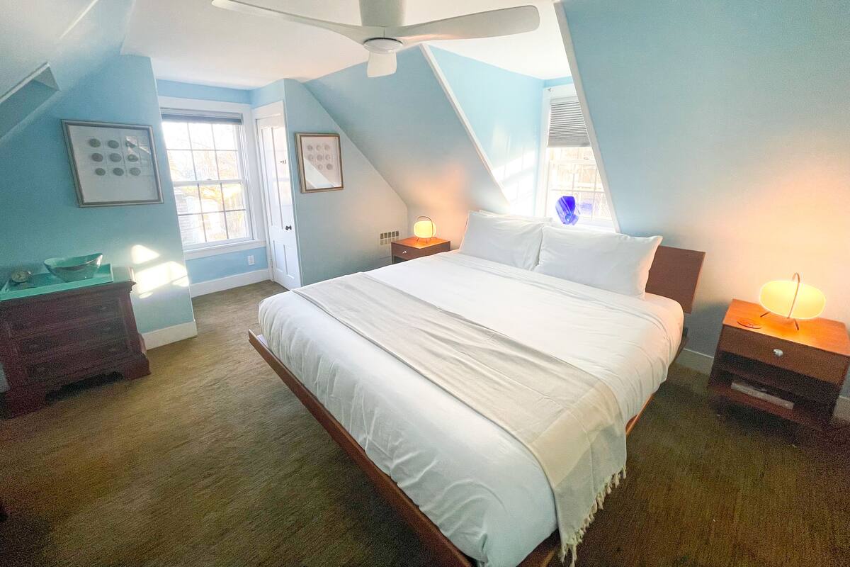 A bedroom with a large bed, a ceiling fan, and a window with blinds.