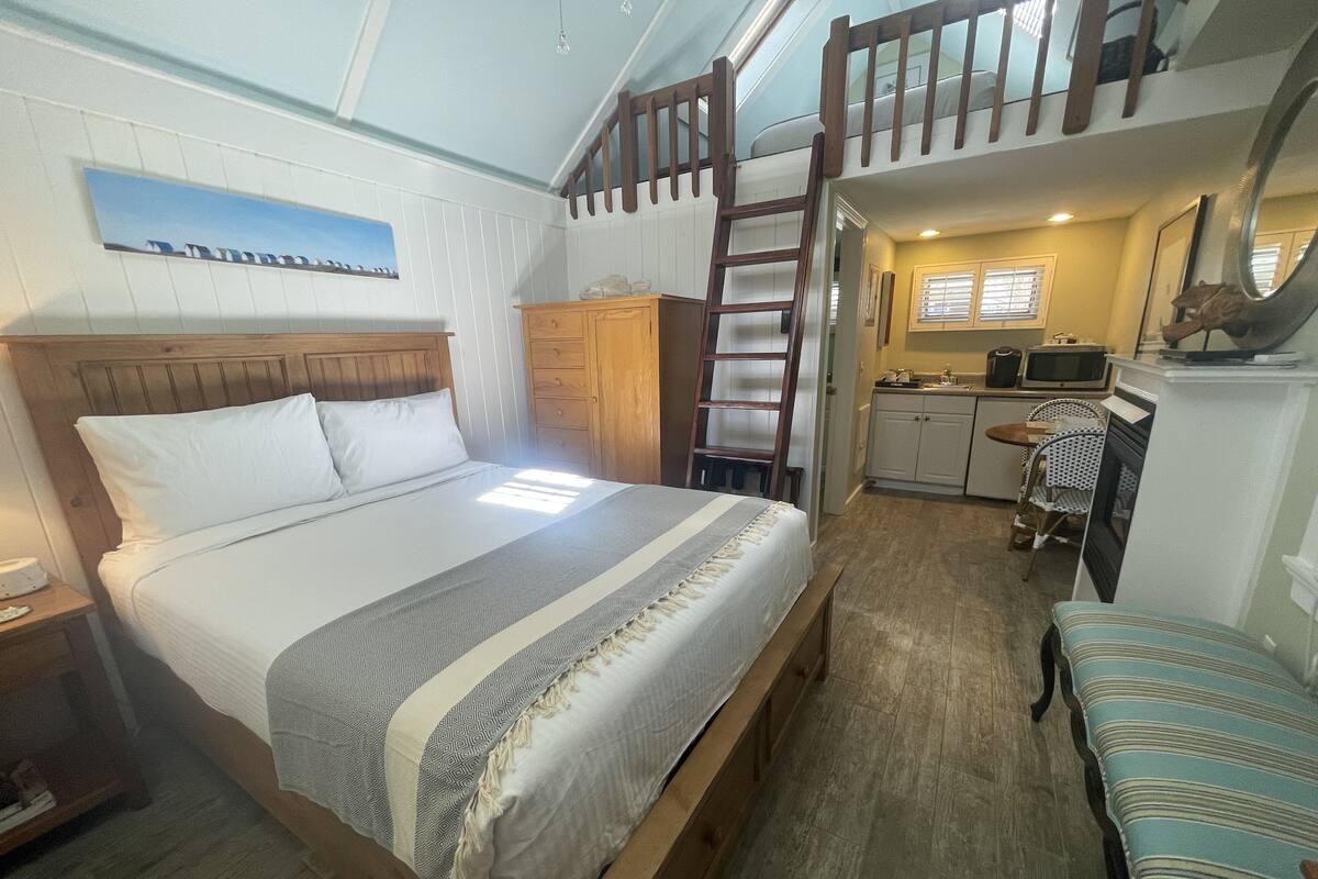 A bedroom with a bed, a wooden ladder, a kitchenette, and a small seating area.