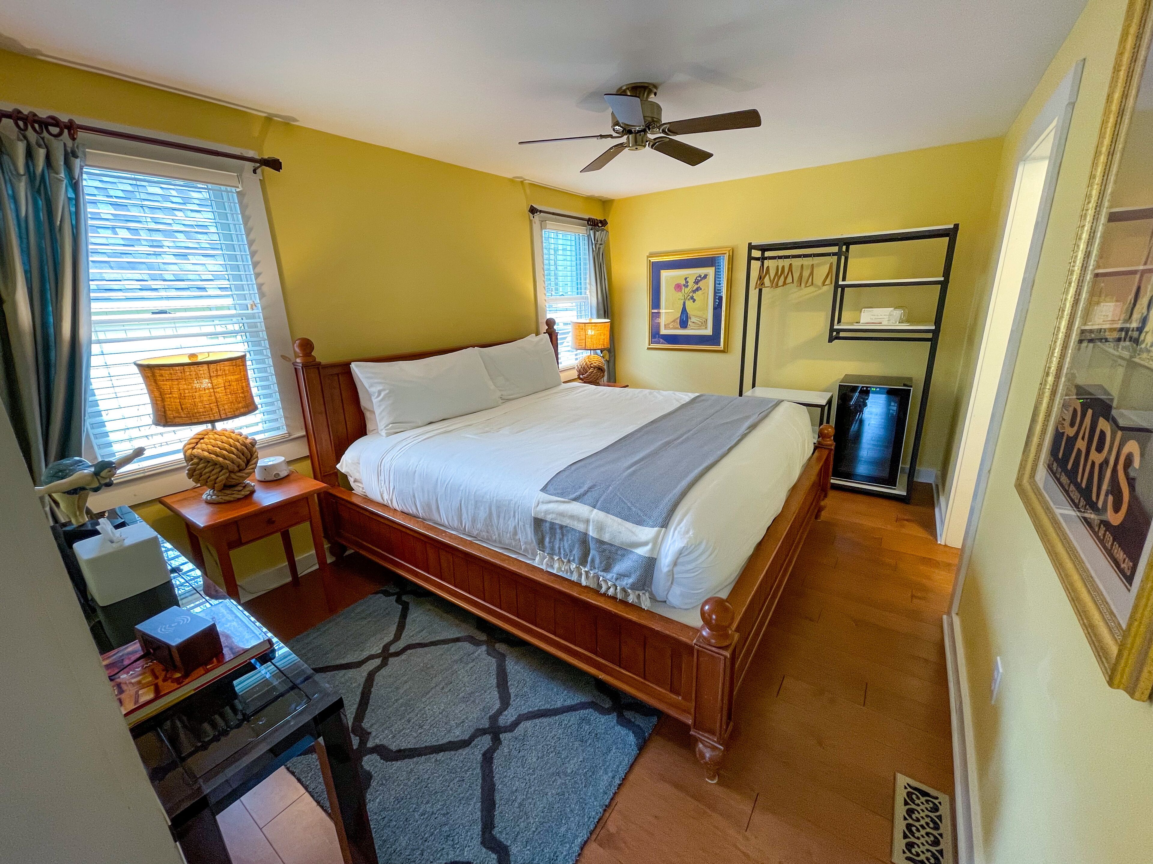 Quarto com cama de madeira, ventoinha no teto, escrivaninha com abajur e quadro pendurado na parede.