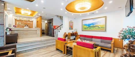 A hotel lobby with a reception desk, seating area, staircase, and artwork.