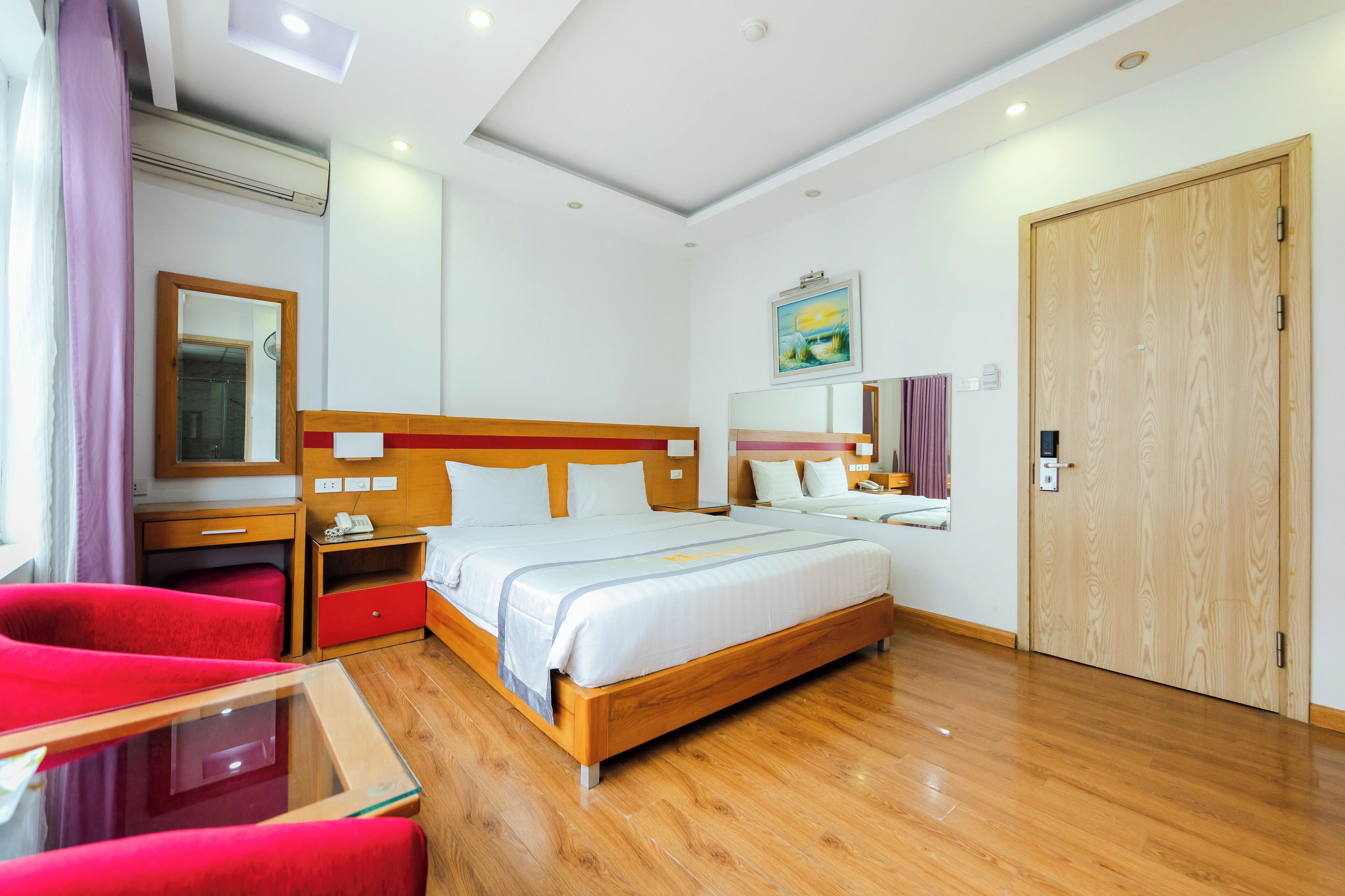 Une chambre d’hôtel avec un lit en bois, des chaises rouges, une petite table, une table de chevet et une porte en bois.