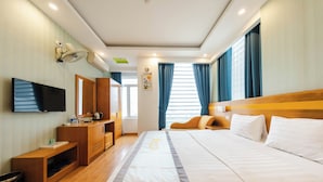 Una habitación de hotel con una cama grande, un televisor, un escritorio con silla y un ventanal con cortinas.