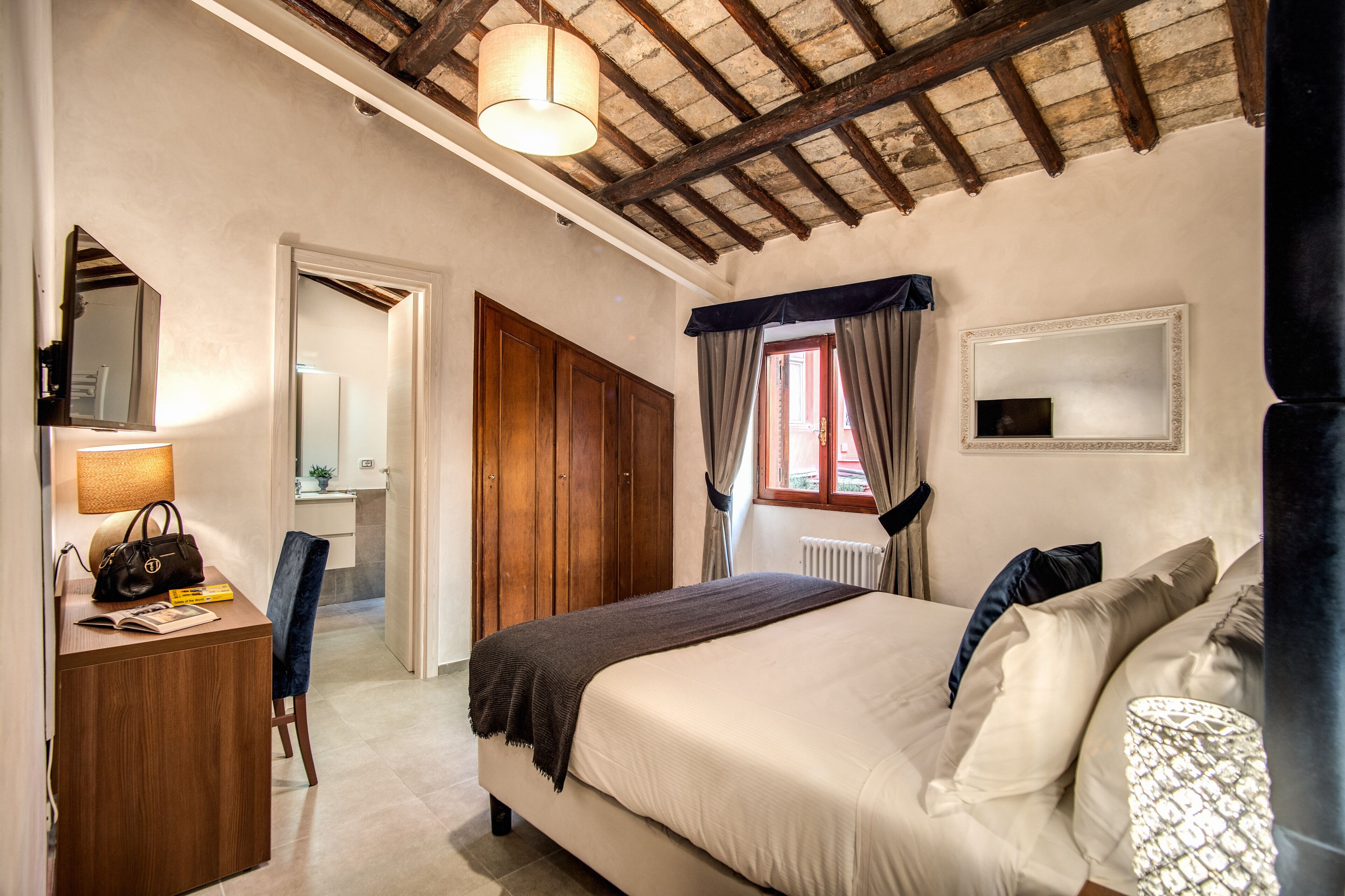 Quarto com cama, escrivaninha com cadeira, espelho e janela com cortinas.