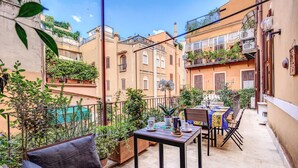 A cozy outdoor patio with a table set for dining, surrounded by potted plants and a comfortable seating area. - Tritone Top House (Rome)