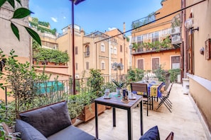 Une agréable terrasse extérieure, avec une table dressée pour les repas, entourée de plantes en pot et agrémentée d’un coin salon confortable.