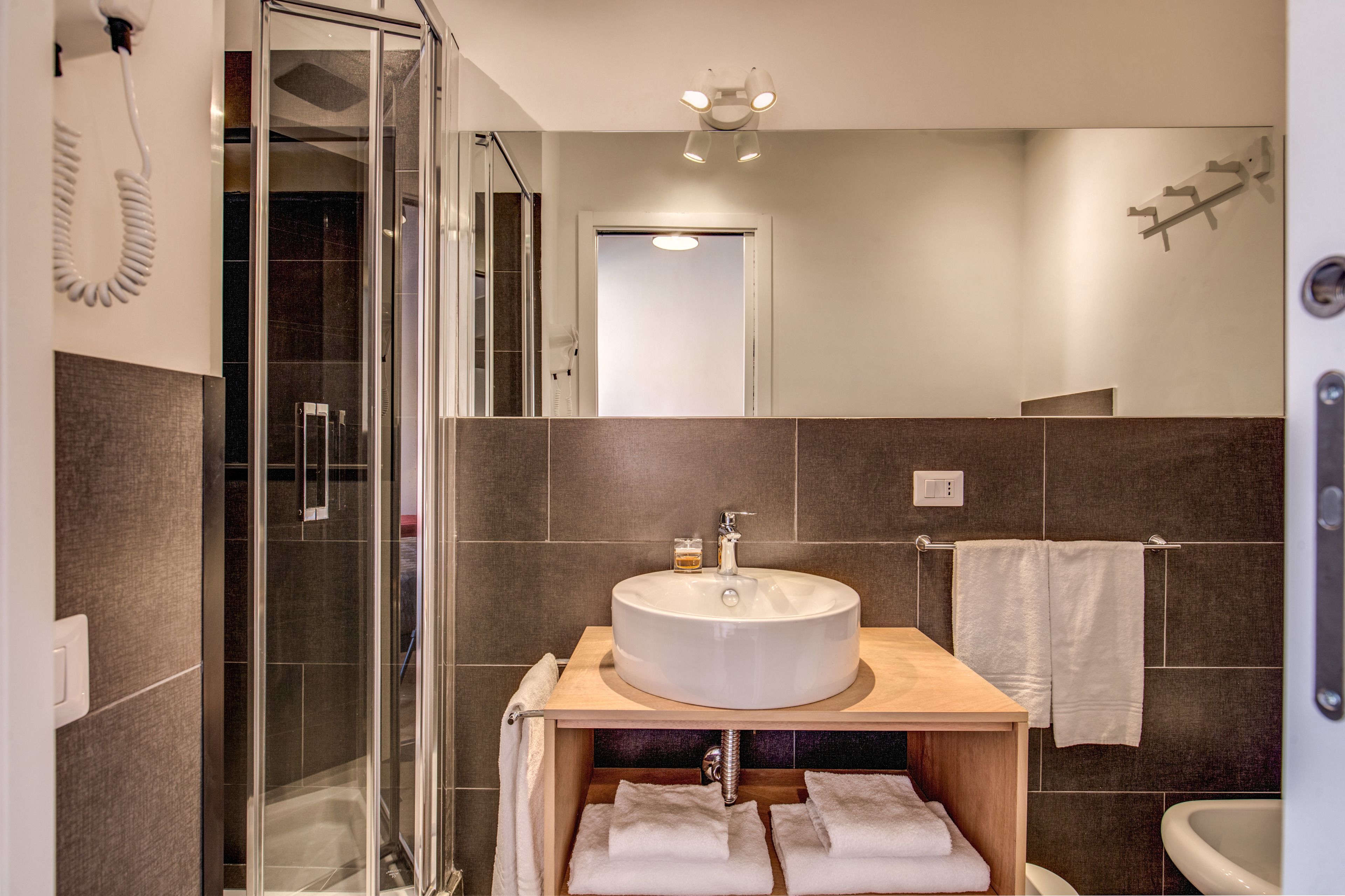 A modern bathroom with a glass-enclosed shower, a wooden vanity with a sink, and a white towel rack.