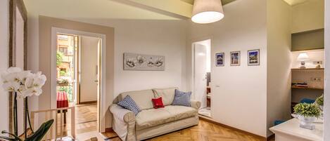 A spacious living room with a wooden herringbone floor, a beige sofa with patterned cushions, a wooden coffee table, and a hanging light fixture.