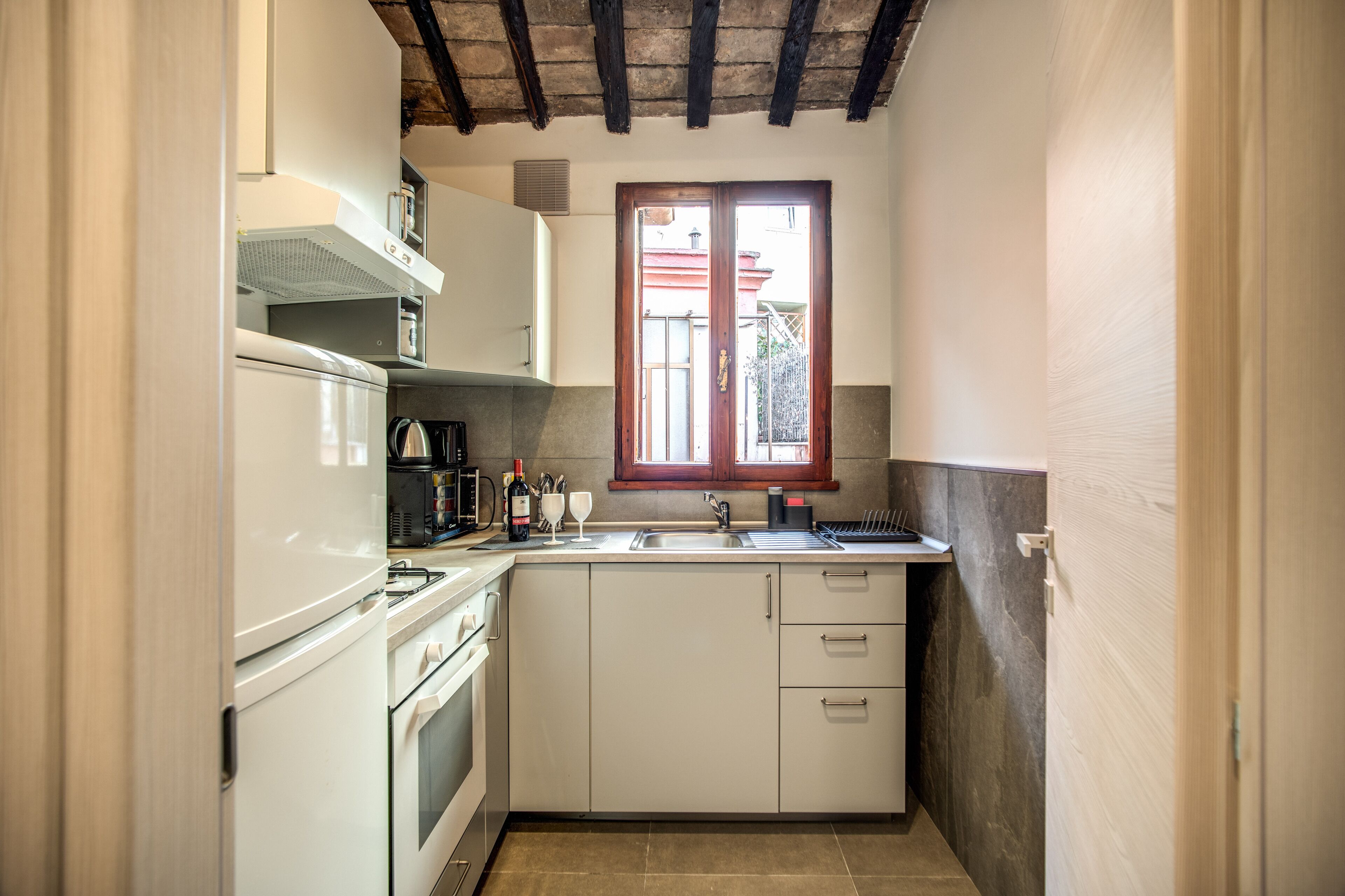 A compact kitchen with white cabinets, a built-in oven, a microwave, and a window above the sink.