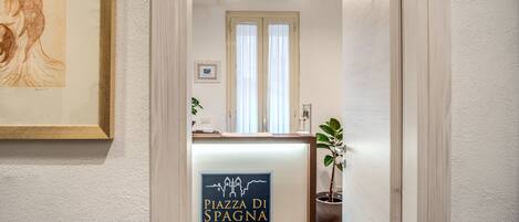Un comptoir d’accueil avec une enseigne indiquant « Piazza Di Spagna Comfort Rooms » et une œuvre d’art encadrée accrochée au mur.