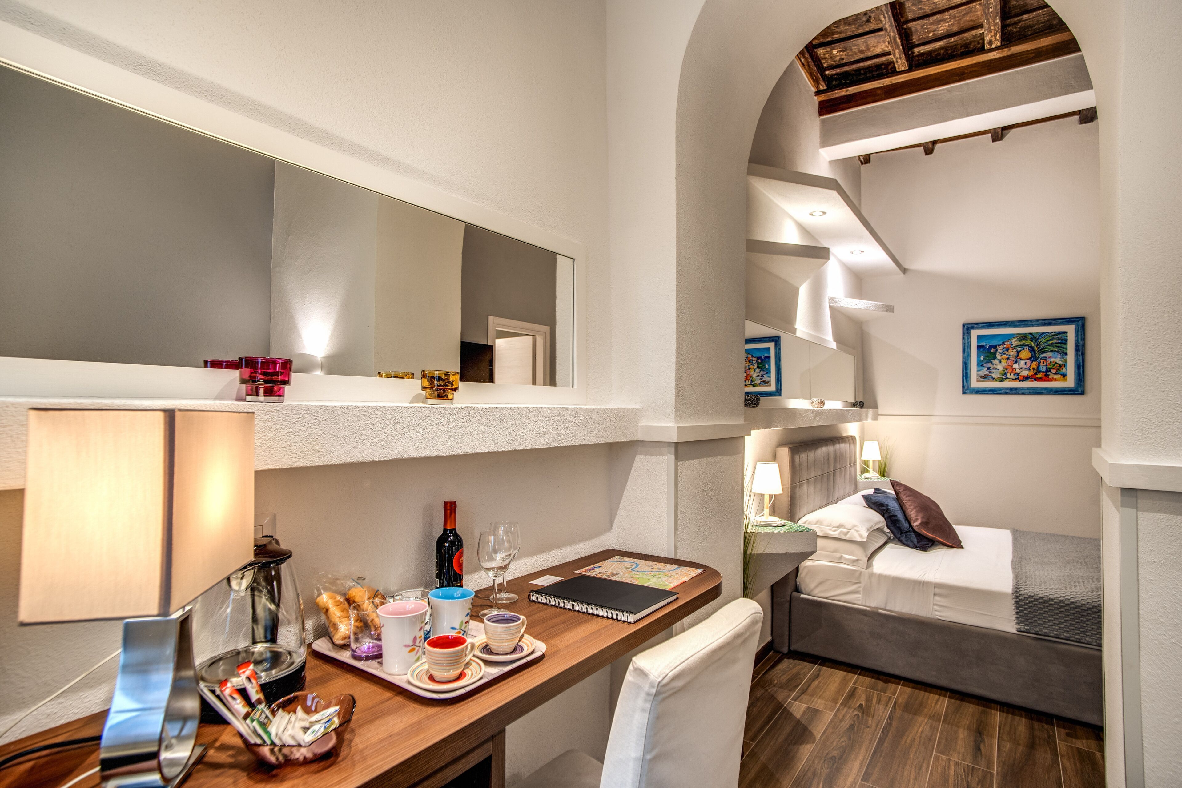 A hotel room with a bed, a desk with a lamp, a mirror, and a breakfast tray.