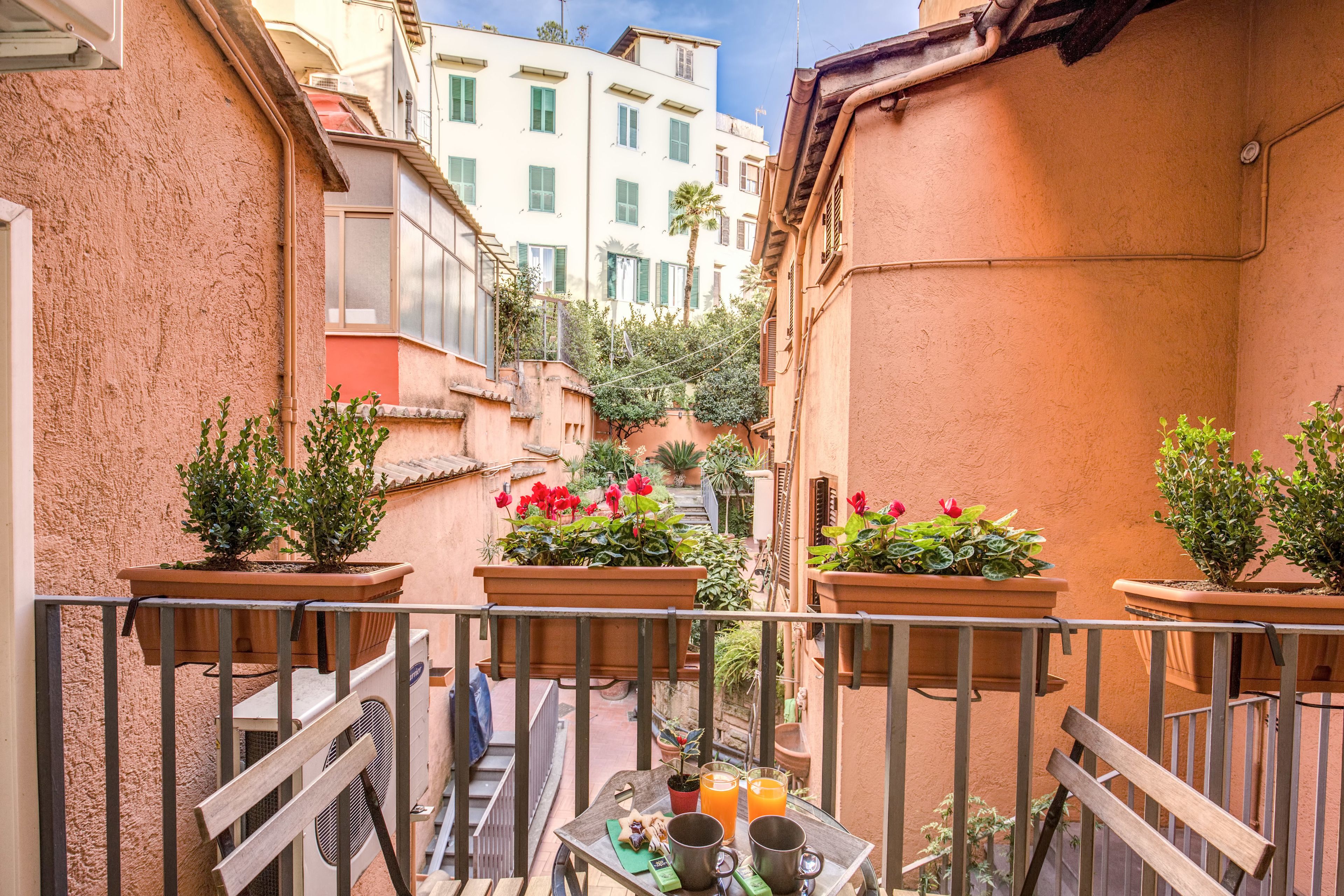 A narrow alleyway with terracotta walls, potted plants, and a table with a chair.
