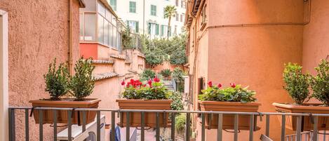 A narrow alleyway with terracotta walls, potted plants, and a table with a chair.