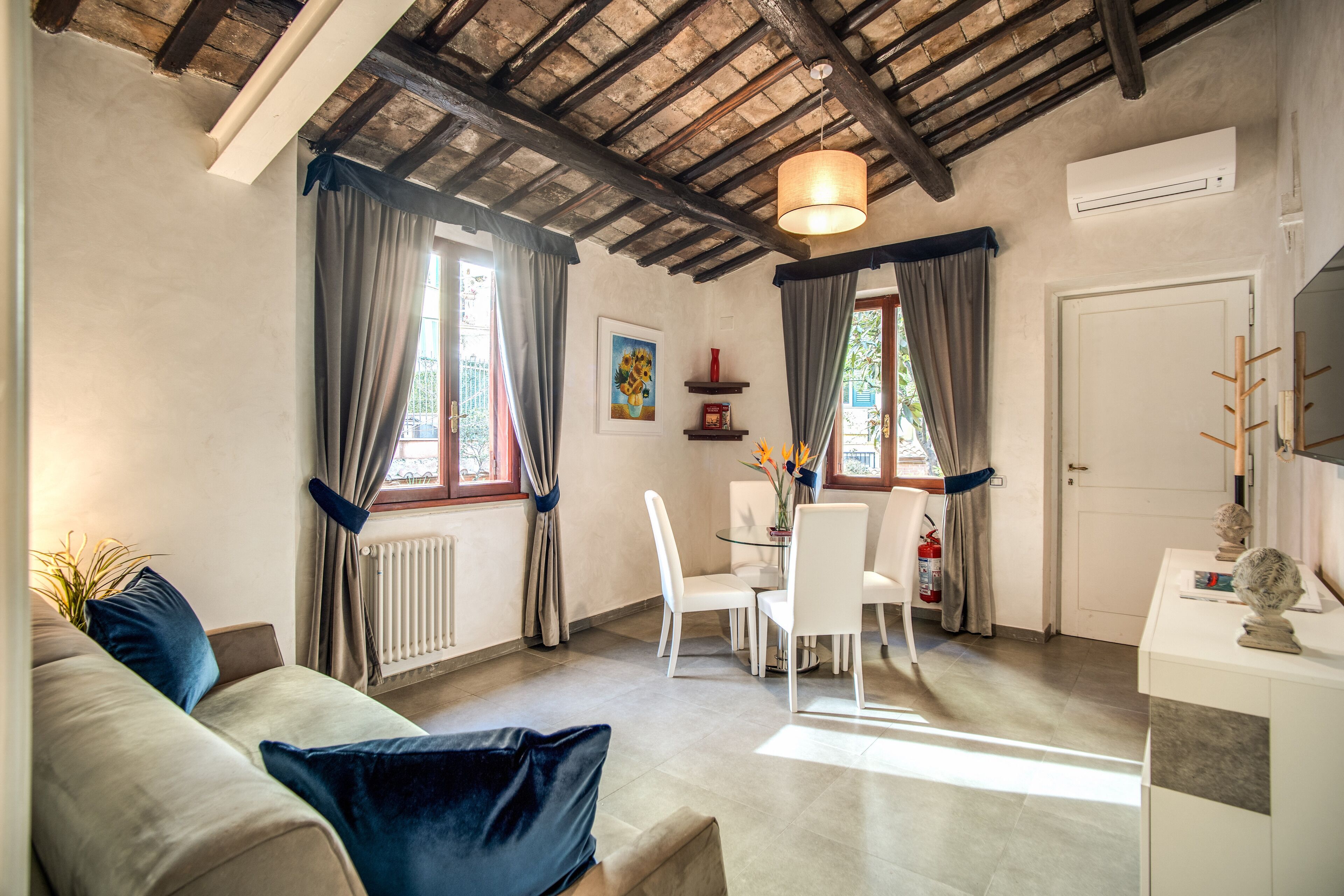 Un salon comprenant un canapé, une table à manger et des chaises. On y trouve une fenêtre avec des rideaux, un radiateur et un ventilateur de plafond.