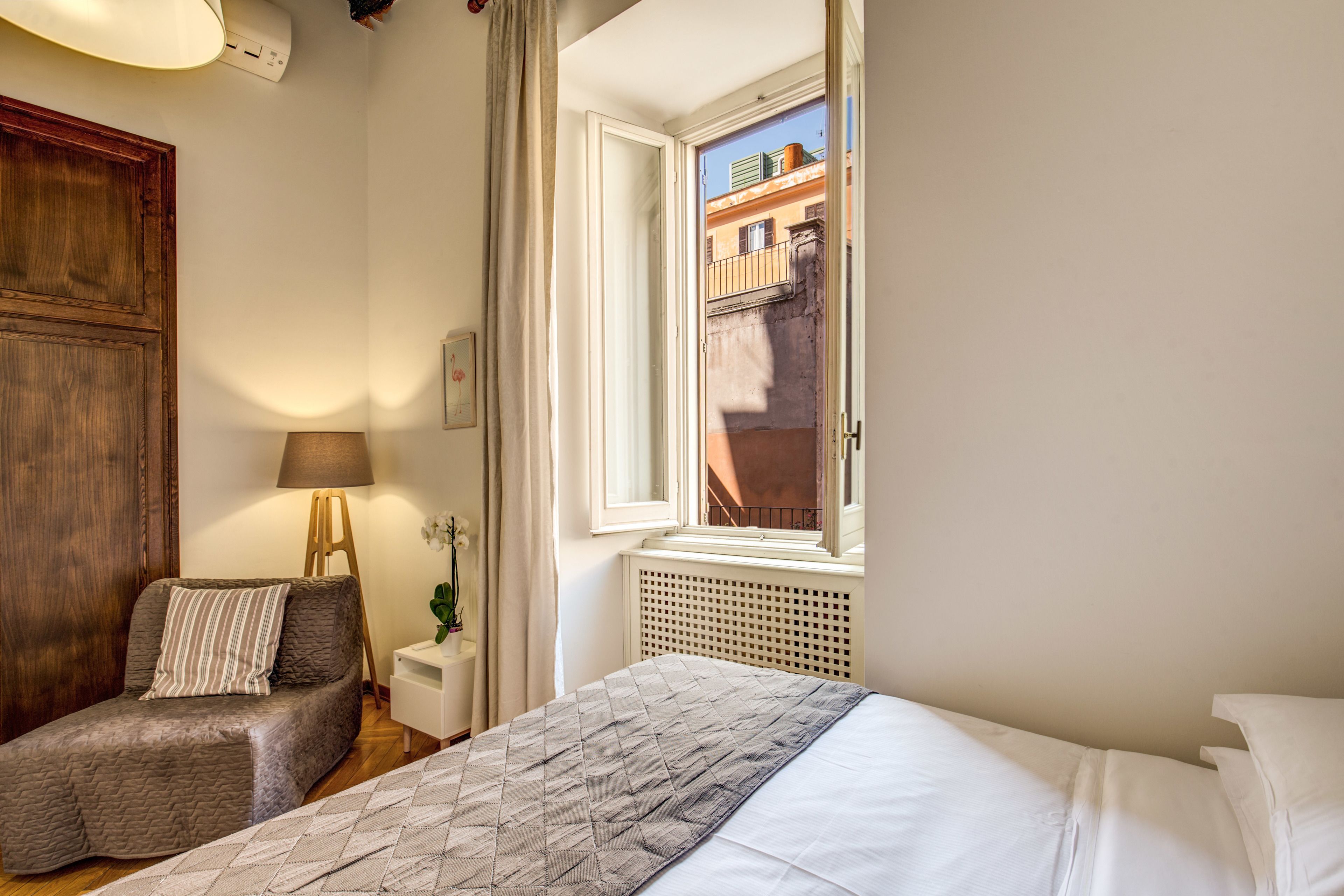 A bedroom with a bed, a chair, a lamp, a window, and a radiator.