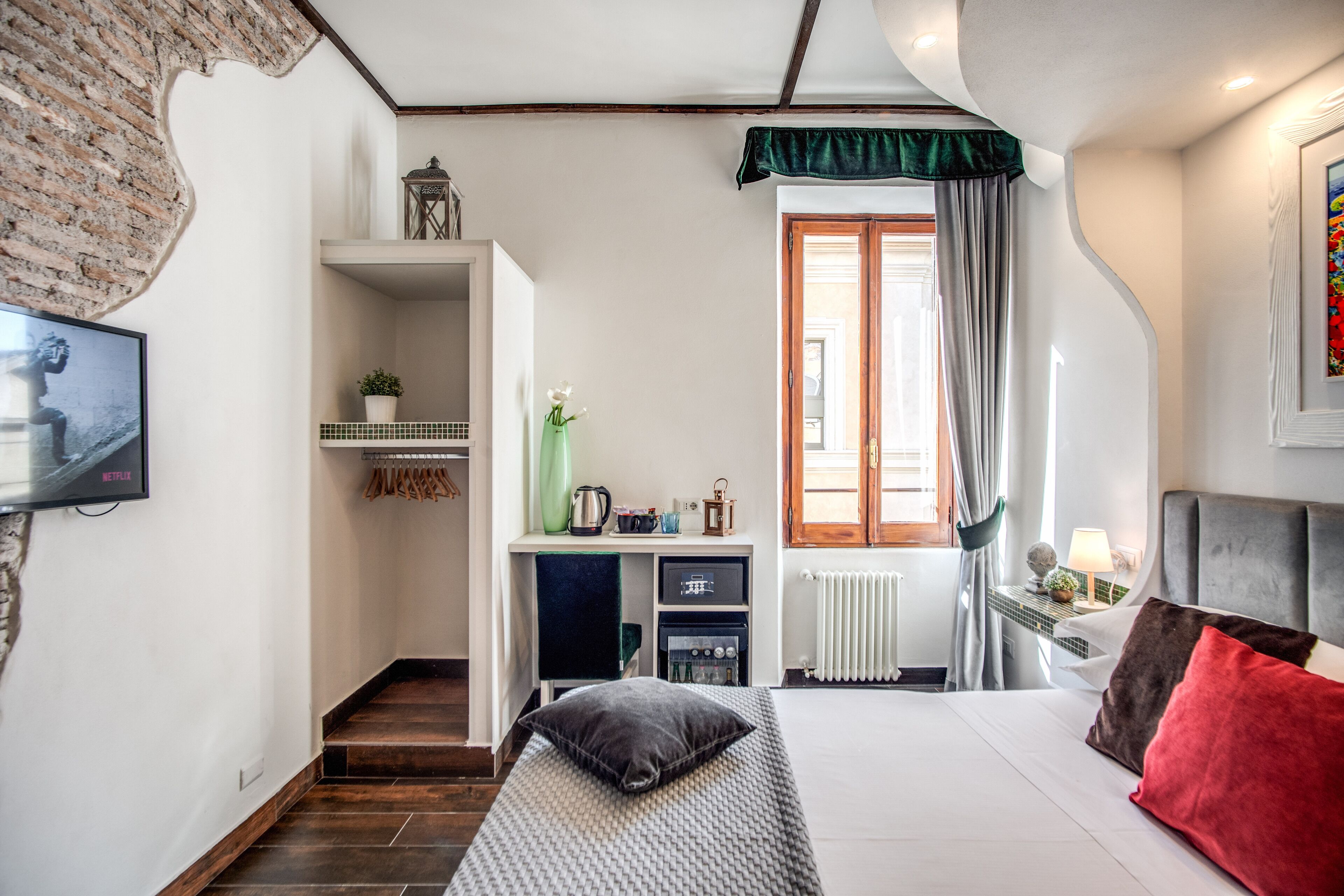 A bedroom with a bed, a desk, a radiator, and a window with curtains.