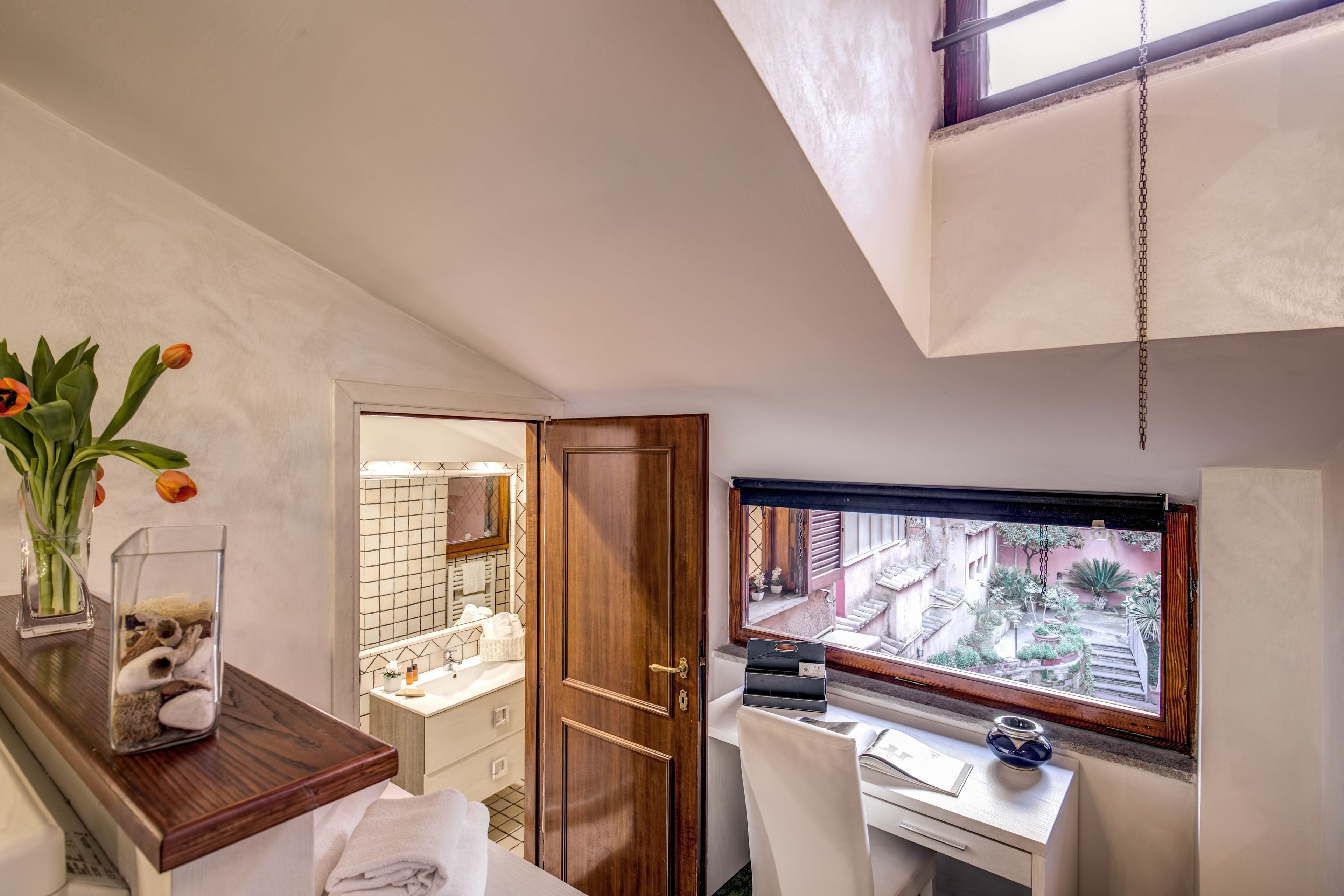 Une salle de bain avec un meuble-lavabo en bois, un miroir, une fenêtre donnant sur l’extérieur et un vase rempli de fleurs posé sur le plan de toilette.
