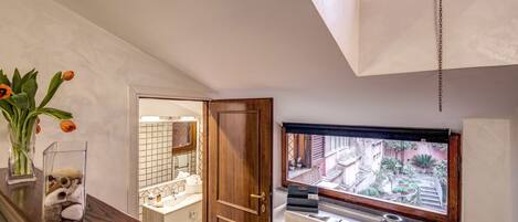 Une salle de bain avec un meuble-lavabo en bois, un miroir, une fenêtre donnant sur l’extérieur et un vase rempli de fleurs posé sur le plan de toilette.