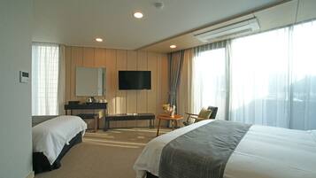 A hotel room with two beds, a desk, a chair, a TV, and large windows with curtains.