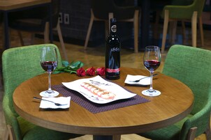 A round wooden table with a bottle of wine, two glasses of red wine, a plate of food, and a bouquet of roses.