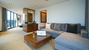 Una sala de estar moderna con un sofá, una mesa de centro y una computadora portátil. Hay una ventana grande con cortinas y vistas al exterior.