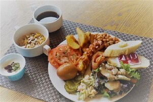 Un plato con un sándwich, tomate, huevo y ensalada, acompañado de dos tazas de café y un recipiente pequeño de semillas.