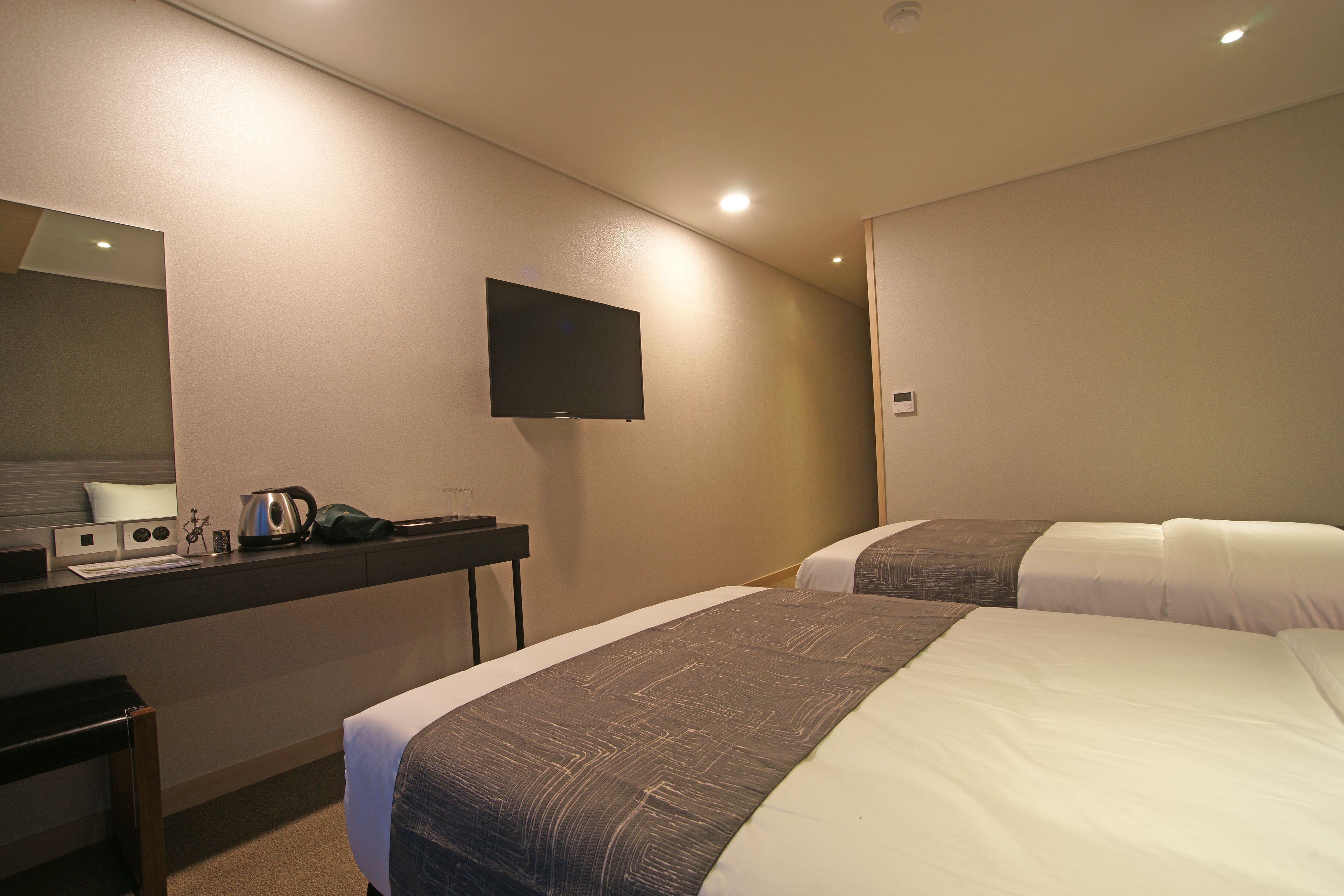 Ett hotellrum med två sängar, ett skrivbord med en platt-TV, en kaffebryggare och ett litet bord med en lampa.