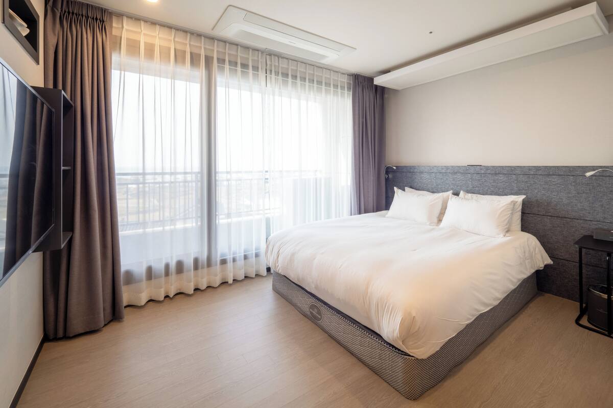 A modern hotel room with a large bed, a flat-screen TV, and a balcony view.