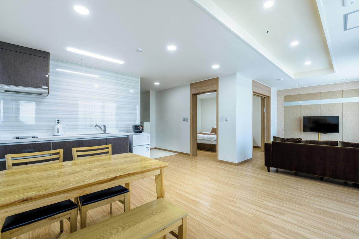A modern kitchen with a dining area, a sofa, and a TV in a living room.