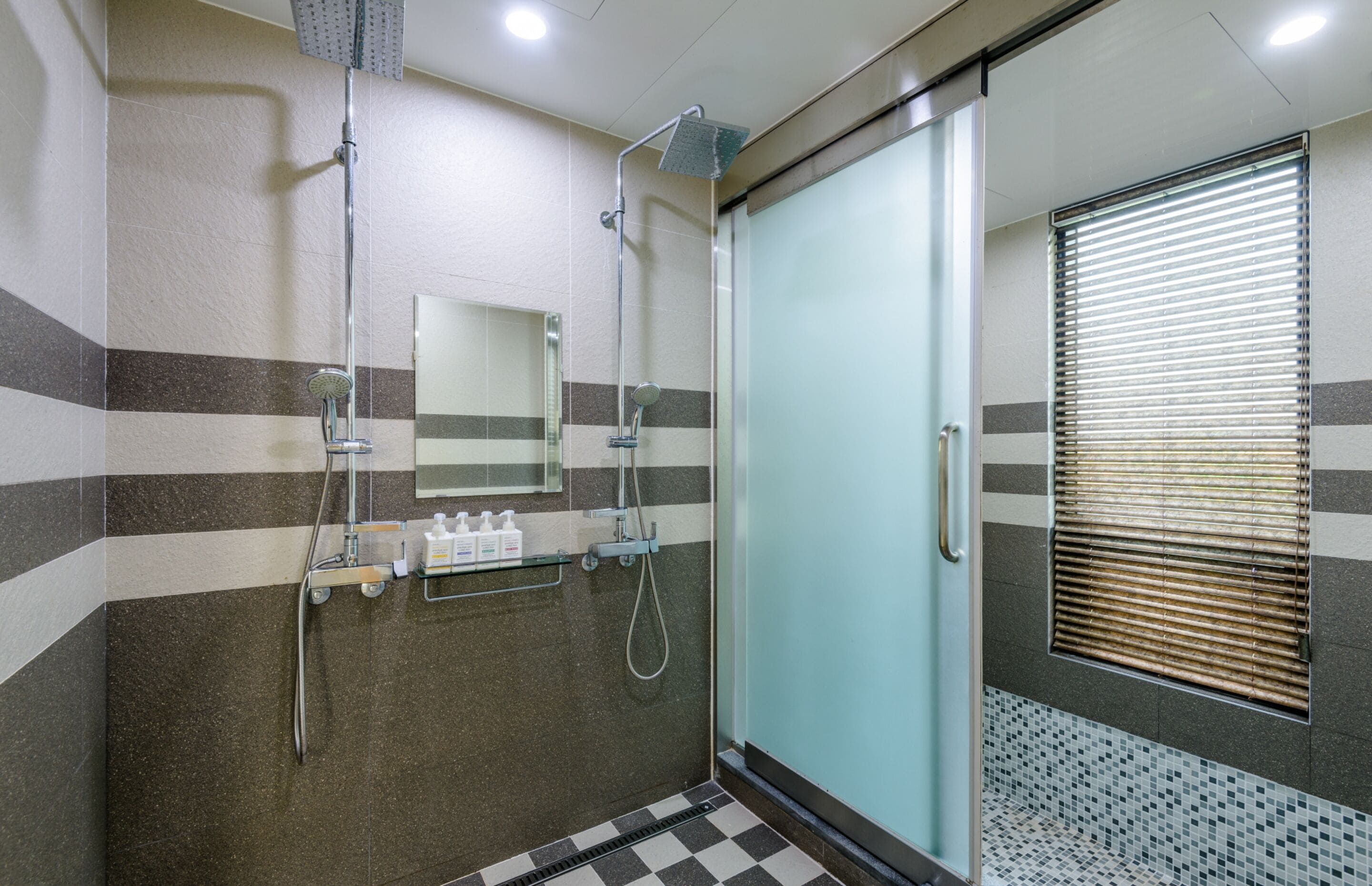 Uma casa de banho moderna com cabine de duche em vidro, espelho e chão em mosaico.
