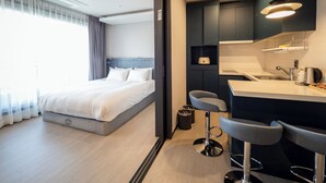 Moderni hotellihuone, jossa on suuri sänky, pieni keittiö ja baarialue.