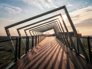 Una terraza de madera con barandillas de metal y paneles de vidrio, que ofrece vistas del paisaje.