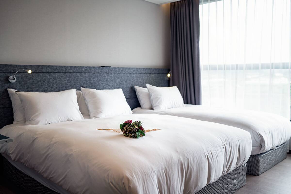 A hotel room with two beds, a grey headboard, white bedding, and a small floral arrangement on the bed.