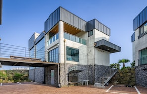 Un edificio moderno de varios pisos con fachada de piedra, ventanas amplias y una zona de estar exterior cubierta.