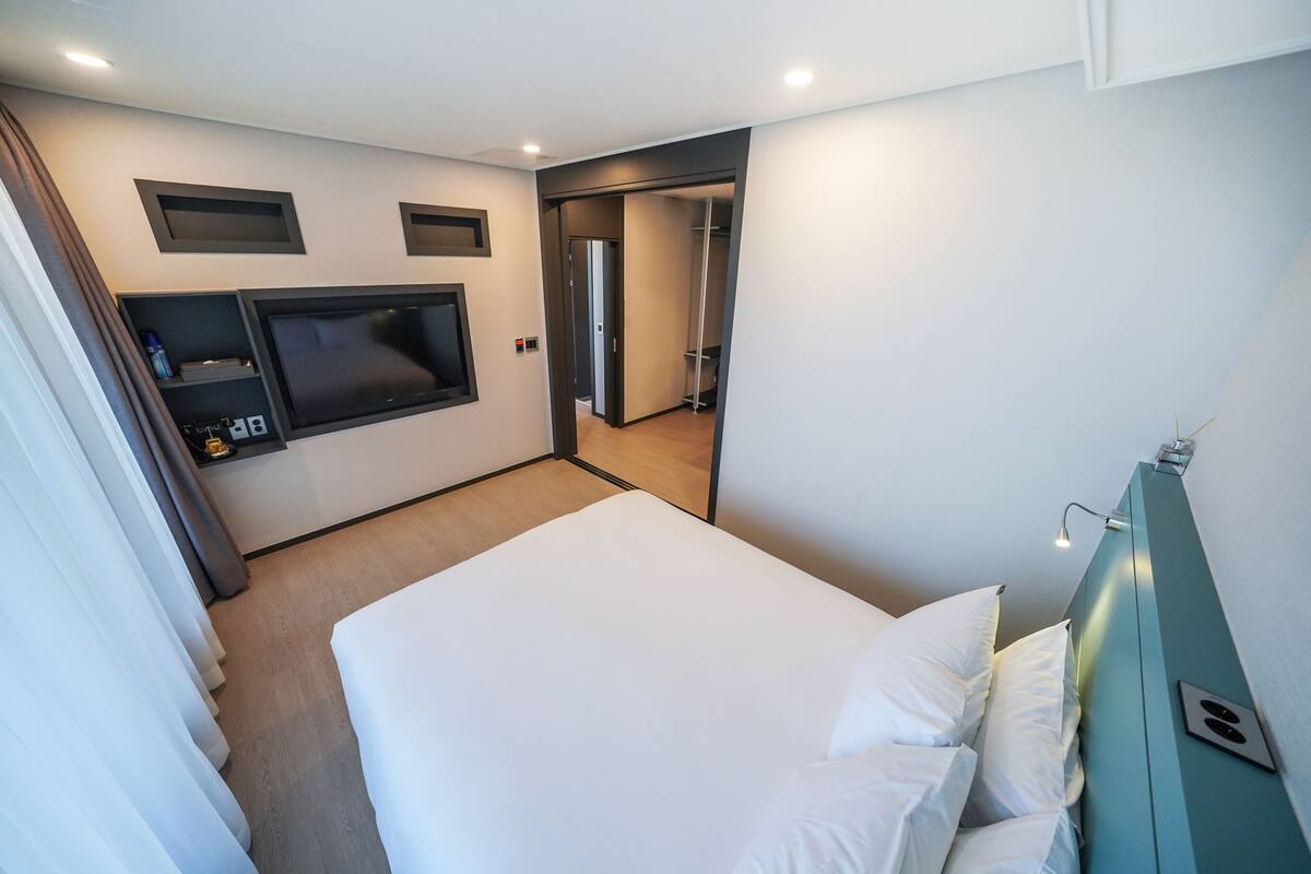 A modern hotel room with a large bed, a TV mounted on the wall, and a walk-in closet.