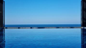 Una piscina infinita con vista despejada al océano y una costa lejana.