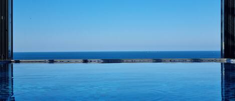 An infinity pool with a clear view of the ocean and a distant shoreline.