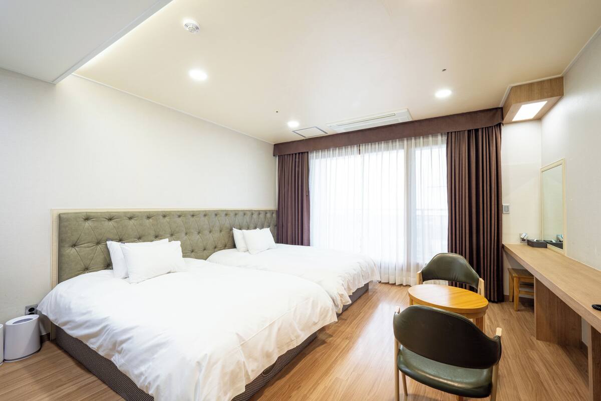 A hotel room with a large bed, a desk, a chair, and a window with curtains.